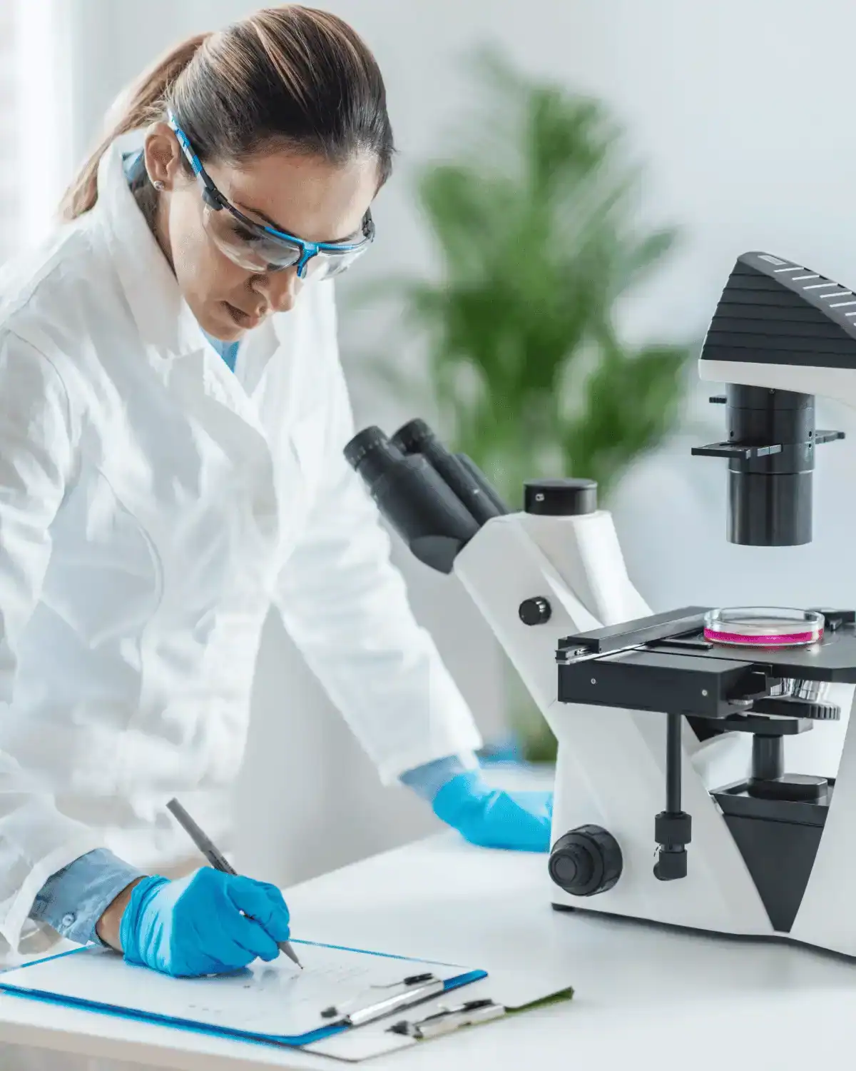 Female scientist using a microscope in a laboratory setting, focusing on medical device development and regulatory compliance.