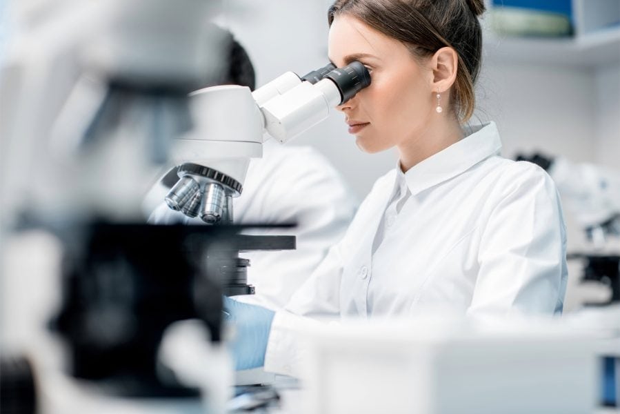 Precise woman researcher examining biological sample using microscope in a laboratory, representing innovative MedTech developments.