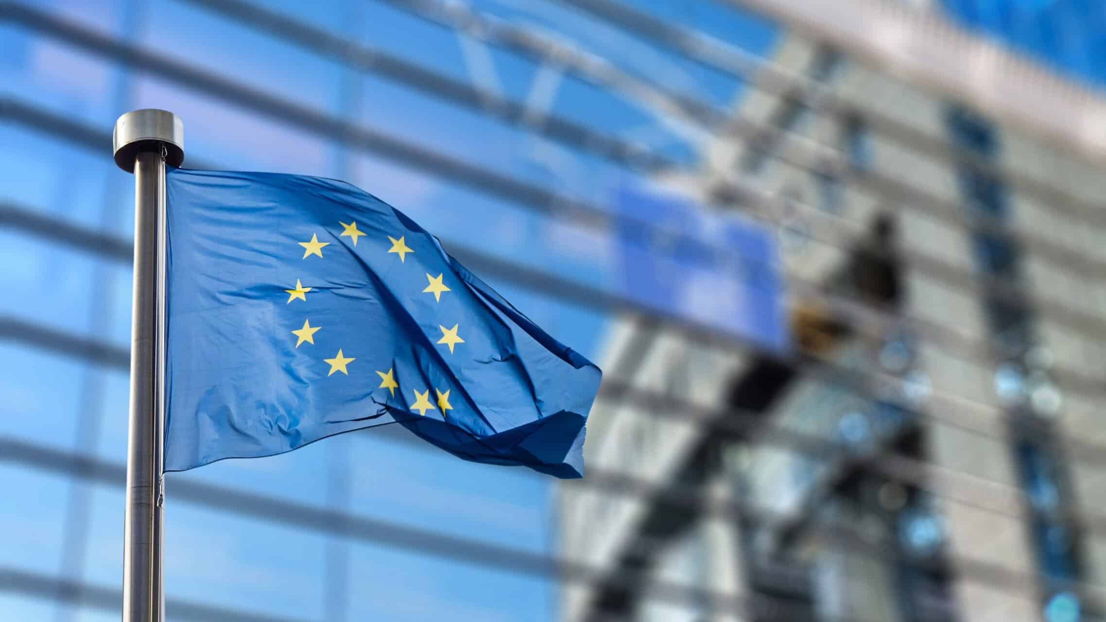 European Union flag waving in front of a modern glass building, symbolizing medtech innovation and European healthcare advancement.