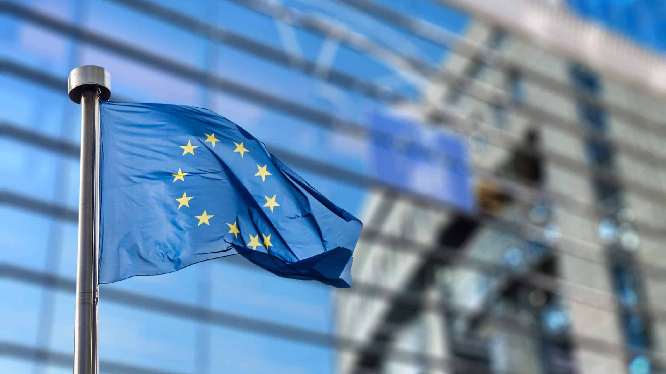 Europe flag flying in front of a modern glass building, symbolizing EU leadership and innovation in MedTech industry, highlighting the impact of the EU on accelerating medical technology advancements.